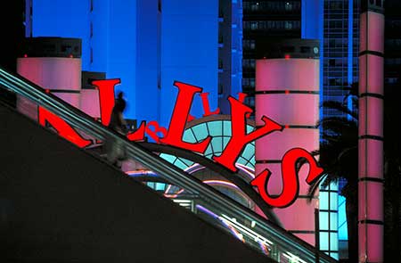 A brightly lit urban scene featuring neon lights at the Las Vegas Hotel Ballys. A blurred silhouette of a person on an escalator appears in the foreground. The background shows colorful illuminated buildings at night. It illustrates how we use the overlapping of objects as a clue to perceive spatial depth.