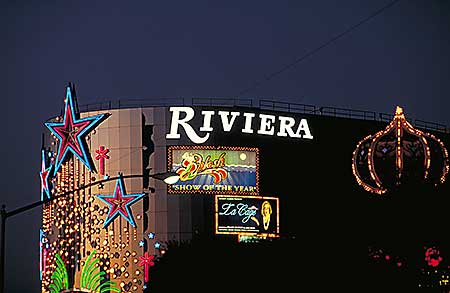 Neon-lit facade of the Riviera Hotel and Casino in Las Vegas at night, featuring large illuminated stars and signs. The signage includes Riviera in bold letters and vibrant advertisements for shows, including one with The Comedy Club text. It is an example of an image with little depth effect due to no atmospheric perspective.