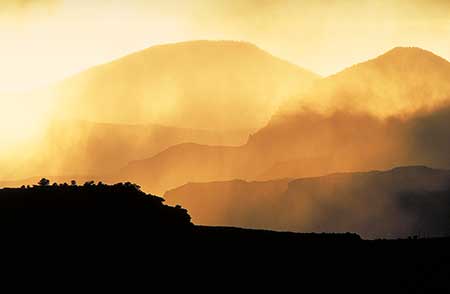 A landscape with layers of misty hills and mountains in Capitol Reef National Park at sunset, casting a golden hue. Silhouettes of trees are visible on the nearest hill, creating a serene and atmospheric scene. It is an example of an image that uses clearly recognizable planes to create spatial depth.