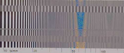 A blurry image of a test pattern with alternating black and white vertical lines that gradually increase in frequency from left to right. There is a blue and orange distortion in the center. A horizontal axis shows numbers from 10 to 50.
